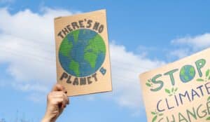 Hand holding up DIY cardboard sign with an earth in the centre and saying "There's no planet B".