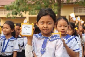 Young student in Cambodia smiling and holding up their new JuniorBuddy solar light to help them study after dark.