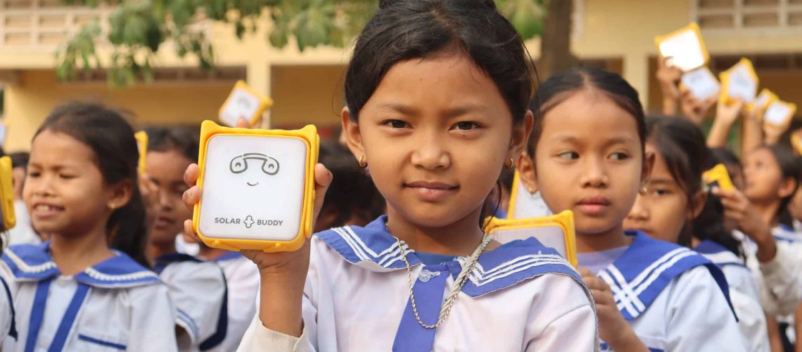 Young student in Cambodia smiling and holding up their new JuniorBuddy solar light to help them study after dark.